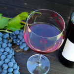 A glass of red wine and a bottle and some grapes