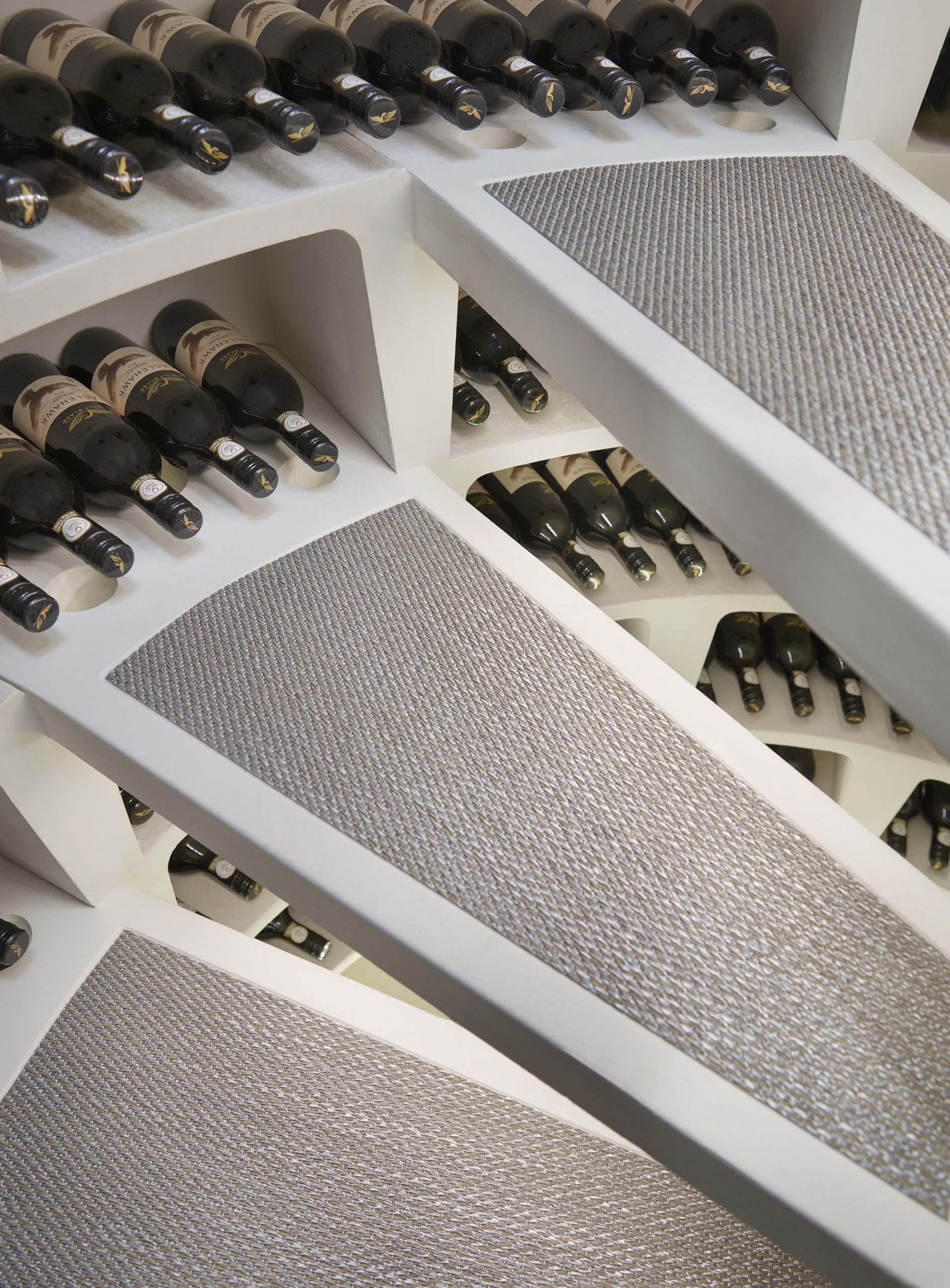 close up of the stairs descending into a spiral cellar with wine bottles shown stored around the edges